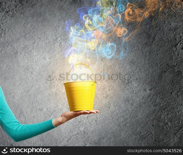 Painting concept. Close up of female hand holding bucket with colorful fumes