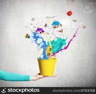 Painting concept. Close up of female hand holding bucket with colorful splashes