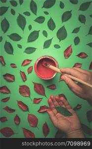 Painting green leaves with red paint from a can. Man&rsquo;s hand painting with a pencil the leaves in red