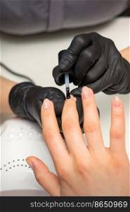 Painting nails of a woman. Hands of Manicurist in black gloves applying transparent nail polish on female Nails in a beauty salon. Painting nails of a woman. Hands of Manicurist in black gloves applying transparent nail polish on female Nails in a beauty salon.