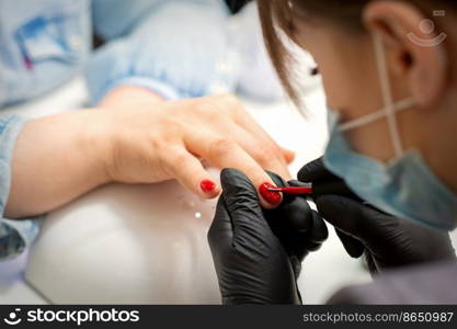 Painting nails of a woman. Hands of Manicurist in black gloves applying red nail polish on female Nails in a beauty salon. Painting nails of a woman. Hands of Manicurist in black gloves applying red nail polish on female Nails in a beauty salon.