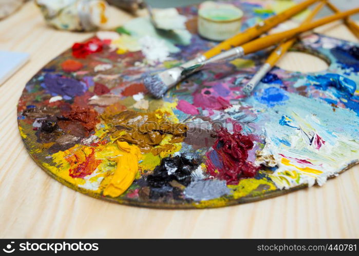 paints, brushes, palette lying on a wooden table