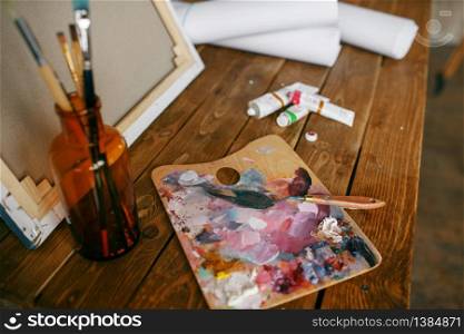 Paints on palette, brush in bottle, canvas, nobody. Painter tools on the table in art studio, equipment on artist workplace, paintbrush, creative atelier or workshop. Paints on palette, brush in bottle, canvas, nobody