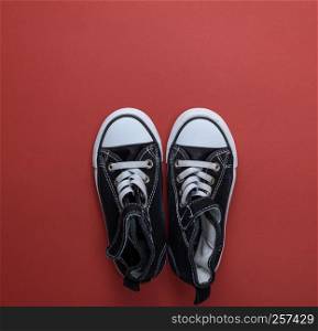pair of black old textile sneakers on a red background, top view