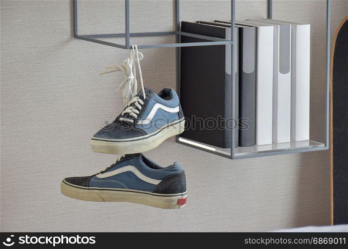 pair of casual blue sneaker shoes hanging on book shelf at home