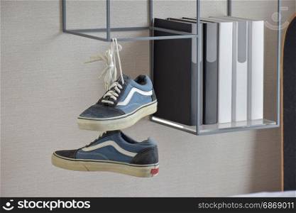 pair of casual blue sneaker shoes hanging on book shelf at home