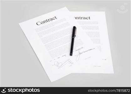 Pair of contracts containing generic text and fictious signatures with a pen on the grey surface of a desk
