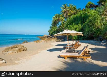 Pair of deck chairs with sun umbrellas at tropical beach with palm trees at sunny day