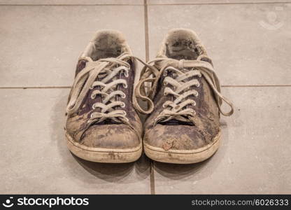 Pair of dirty shoes with mud on the floor