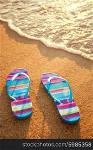 pair of flip-flops on a sandy beach at sunset, holiday and vacation concept