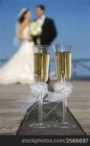 Pair of flute glasses of champagne with Caucasian bride and groom blurred in background.