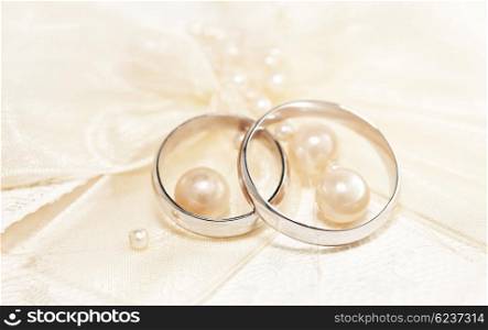 Pair of golden wedding rings over invitation card decorated with silk bow &amp; pearls