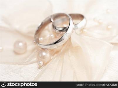 Pair of golden wedding rings over invitation card decorated with silk bow &amp; pearls