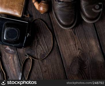 pair of leather brown shoes and an old vintage camera in a case on a wooden background, copy space