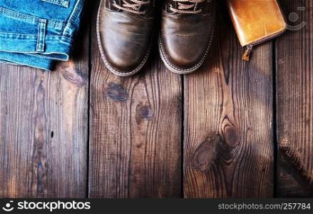 pair of leather brown shoes, wallet and jeans on a wooden background, empty space