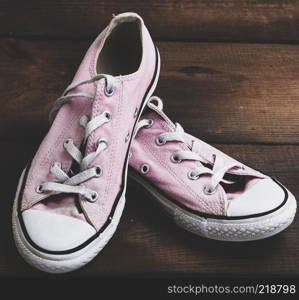 pair of old worn pink sneakers with white laces on a wooden background, vintage toning
