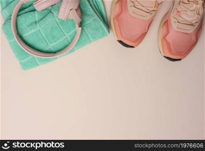 pair of pink textile sneakers, wireless headphones and a textile green towel on a beige background. Set for sports, running