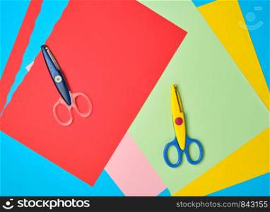 pair of plastic scissors and colored paper for cutting figures, application and scrapbooking
