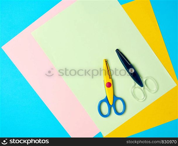 pair of plastic scissors and colored paper on a blue background, back to school backdrop