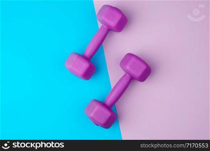 pair of purple plastic dumbbells on a blue-violet background, backdrop for sports