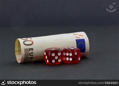 Pair of red dice in front of euro money placed on simple, dark background depicts financial policies and business environments with chance and risk.