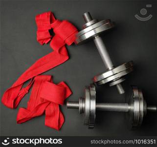pair of shiny steel typesetting dumbbells for bodybuilding and textile bandage on a black background, top view