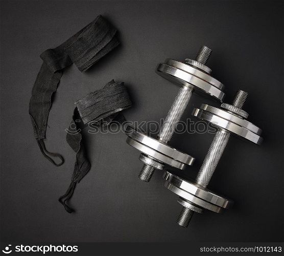 pair of shiny steel typesetting dumbbells for bodybuilding on a black background, top view