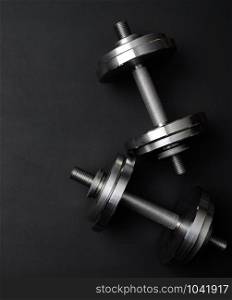 pair of shiny steel typesetting dumbbells for bodybuilding on a black background, top view