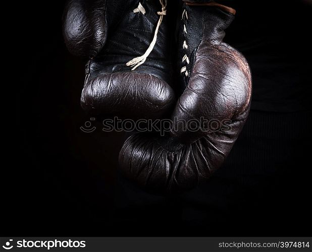 pair of very old brown boxing gloves hanging, black background