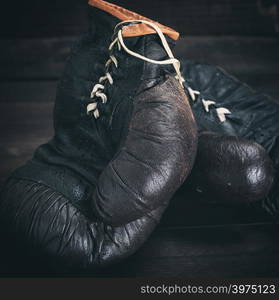 pair of very old shabby black leather boxing gloves on a brown wooden background