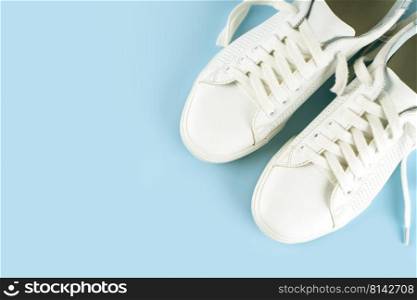 Pair of white sneakers on blue background. Unisex shoes, stylish white sneakers. Top view, flat lay, mockup with copy space for text. White sneakers on blue background