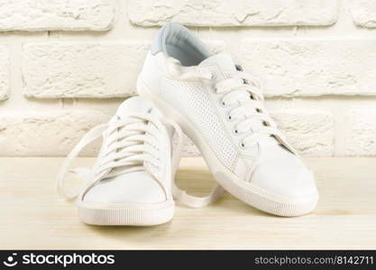 Pair of white sneakers on white brick background. Unisex shoes, stylish white sneakers.. White sneakers on white brick background