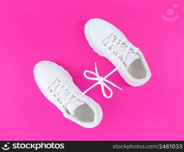 Pair of white sport shoes connected with laces bow on a pink background.. Pair of white sport shoes connected with laces bow on pink background.