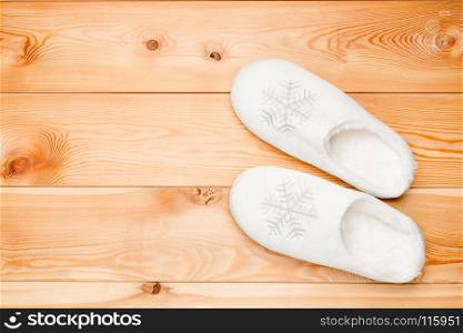 pair of white warm slippers with snowflakes view from above on a wooden floor