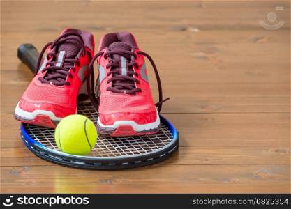 Pair of women's sneakers on a tennis racket on a wooden floor
