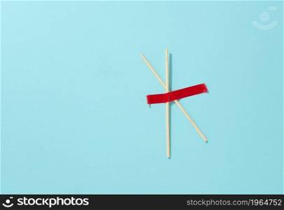 pair of wooden sticks glued with red sticky tape on a blue background, top view