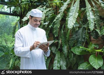 Pakistani business asian man using tablet,standing in green cafe wear muslim dress ,freelance business concept.