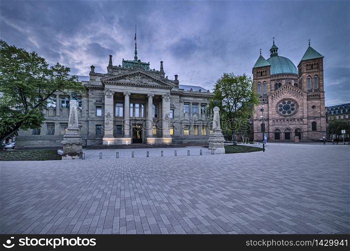 Palais de Justice (Courthouse) next to Saint-Pierre-le-Jeune catholic church in Strasbourg in the evening with dramatic clouds, Alsace Region, France