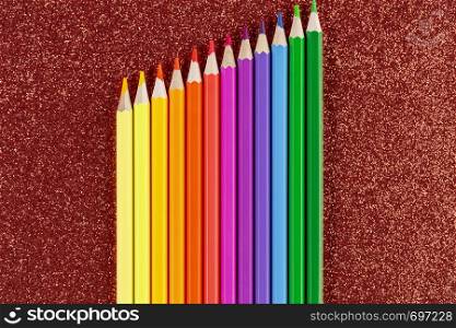 Palette of colored pencils on glitter red background. Colored pencils on glitter red background