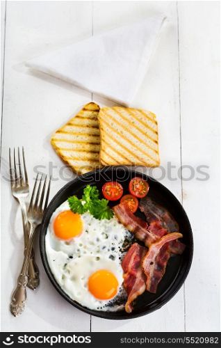 pan of fried eggs, bacon and vegetables on wooden table