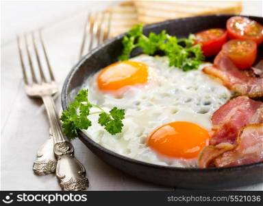 pan of fried eggs, bacon and vegetables on wooden table