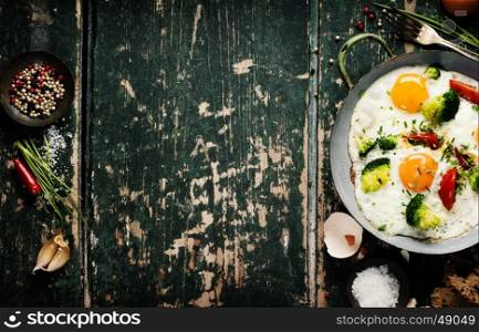 Pan of fried eggs, broccoli and cherry-tomatoes with bread on old green background, top view