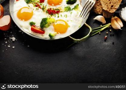 Pan of fried eggs, broccoli and cherry-tomatoes with bread on old metal background, top view