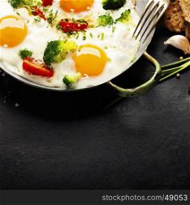 Pan of fried eggs, broccoli and cherry-tomatoes with bread on old metal background, top view
