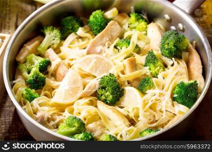 pan of pasta with chicken and broccoli on wooden table