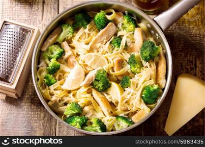 pan of pasta with chicken and broccoli on wooden table, top view