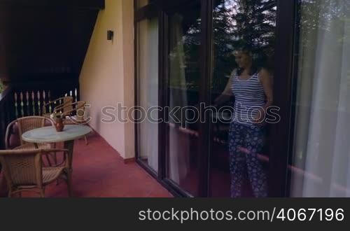 Pan of young woman coming on terrace to relax in the morning. Woman awakened from sleep breathing fresh air on villa balcony in summer.