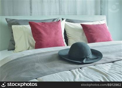 Panama hat setting on bed runner with pillows in deep red, white and gray color