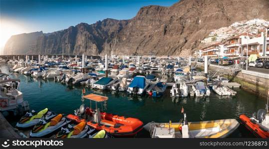 Panaromic photo of port with moored luxurious yachts and motorboats surrounded by high cliffs and mountains. Panaromic image of port with moored luxurious yachts and motorboats surrounded by high cliffs and mountains