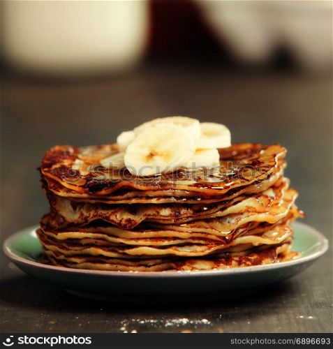 Pancake tower with fresh bananas and honey on a rustic table